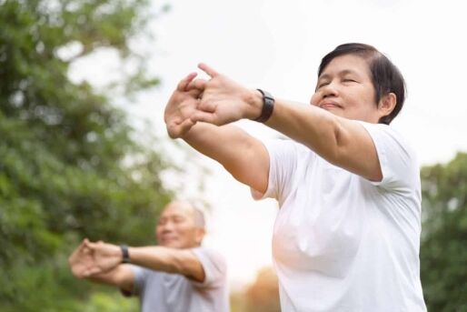 A senior woman and man stretch outside before exercising.